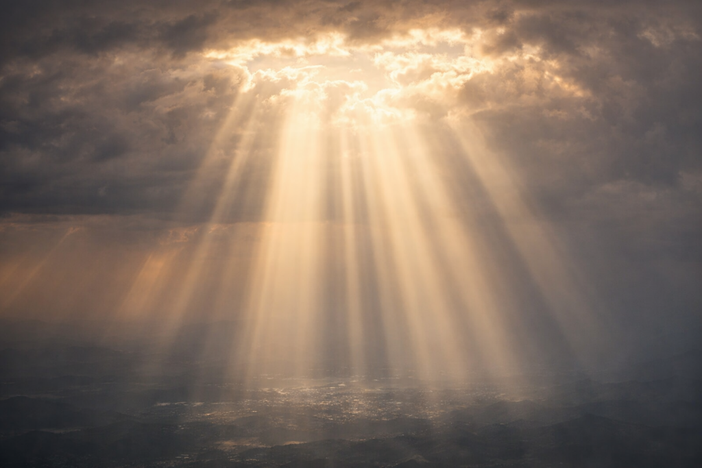 厚い雲の隙間から地上へまっすぐに差し込む光の筋。太陽のように平等に降り注ぐエネルギーを象徴する、静かで神聖な空の風景。